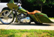 Side picture. Custom olive green bagger motorcycle with a brown leather seat, large front wheel, and low extended saddlebags