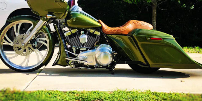 Side picture. Custom olive green bagger motorcycle with a brown leather seat, large front wheel, and low extended saddlebags